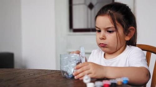 Niña preescolar caucásica haciendo manualidades con botella de plástico y pinturas