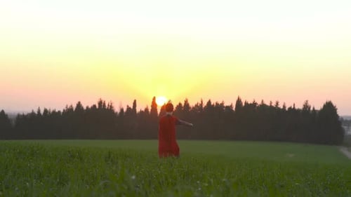 Boy dressed with a Superman cape running in a field, looking into the sunset