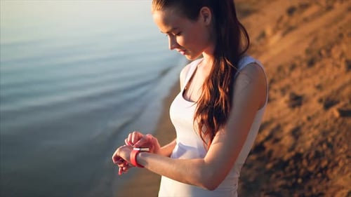 Woman Checking Smartwatch on Ocean Shoreline at Sunset