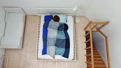 a Top Aerial View of a Person Who is Tossing and Turning in Bed Under a Blanket Trying to Fall