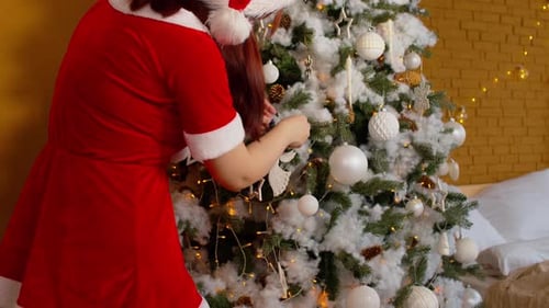 Side View of Woman in Santa Costume Decorating Christmas Tree