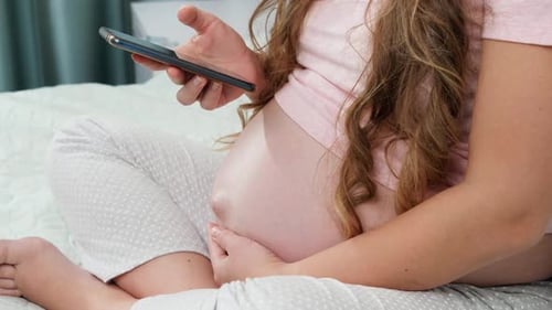 Pregnant Woman Using Phone Resting on Bed