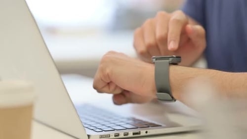 Nahaufnahme männlicher Hände mit Smartwatch bei der Arbeit am Laptop