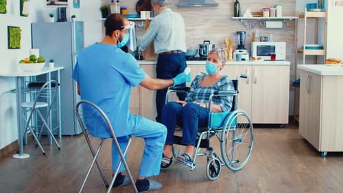 Elderly Couple Home Visit By Geriatrician in Protective Wear