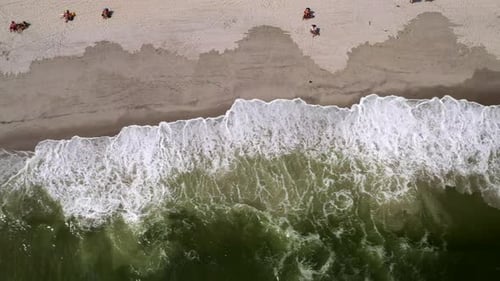 drone bird's eye shot over the beach shoreline, panning left as the waves crash against the shore wi