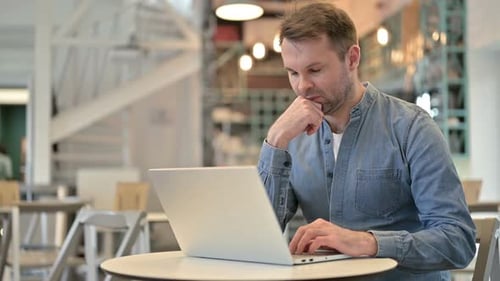 Pensive Casual Man Using Laptop in Cafe