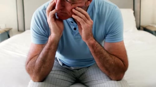 Tensed senior man sitting on bed in bedroom