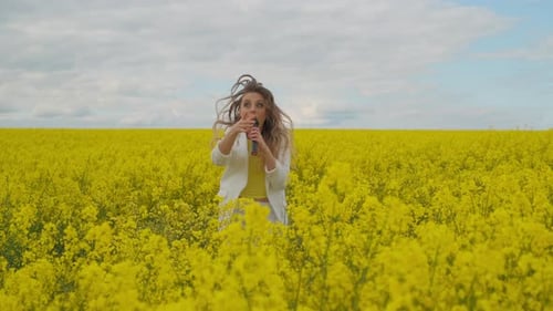 Beautiful Girl Singer in a Yellow Field Dancing and Energizing Looking at the Camera