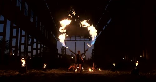 A Group of People with Fire and Torches Dancing at Sunset in the Hangar in Slow Motion