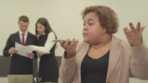 Portrait of Angry Woman in Formal Wear Speaks By Her Cellphone in the Foreground in the Office While