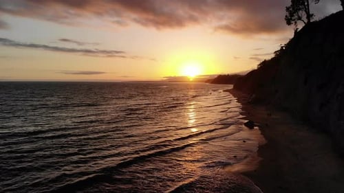 Aerial drone shot of a sunset sky and reflection in the ocean waves near the sandy beach cliffs of S