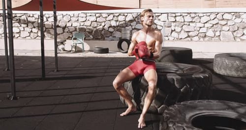 Shirtless Man with Boxing Gloves Sits on Tire