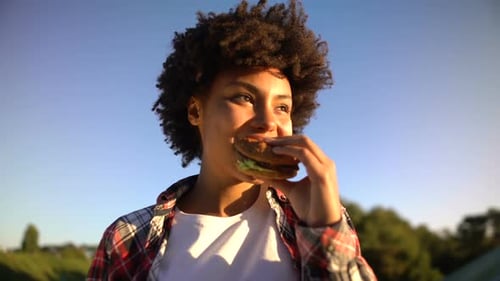 Woman Enjoying a Burger Outdoors on a Sunny Day