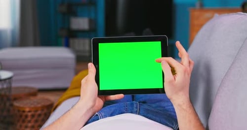 Young Man at Home Uses Green Mockup Screen Digital Tablet