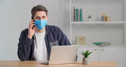 Young Adult Caucasian Male Businessman Wearing Medical Face Mask Sitting in Home Office Table with