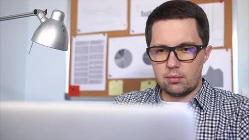 Man Working on Laptop at Desk with Lamp