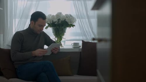 Man Using Tablet Relaxing Indoors Near Window