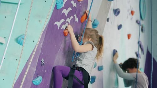 Small Girl and Young Woman Climning Artificial Wall in Gym Focused on Activity