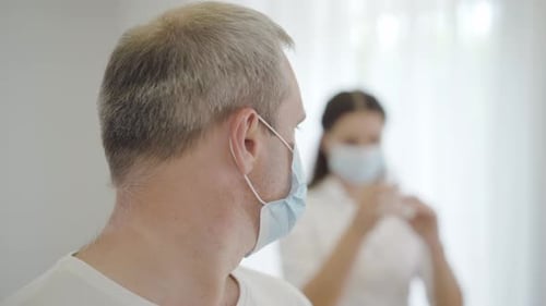 Nahaufnahme eines verängstigten männlichen Patienten in Gesichtsmaske, der auf die Krankenschwester zurückblickt, die Spritze füllt und sich