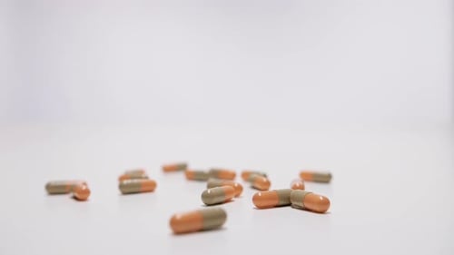Medicine capsules falling on white background in slow motion.