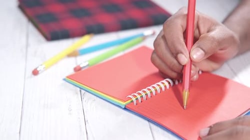 Close Up of Man Hand Writing on Red Color Notepad