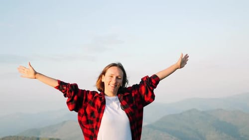 Female tourist standing on the top of hill with hands raised to sides