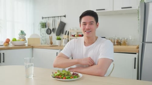 Young Man Eating Salad at Kitchen Table