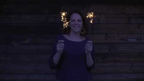 Woman Smiles Holding Sparklers at Night Celebration