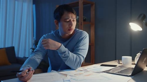 Man Working Late at Desk with Laptop and Documents