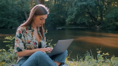 Beautiful girl working on a laptop by the lake