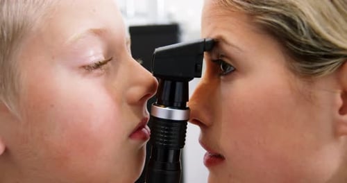 Female optometrist examining young patient with ophthalmoscope