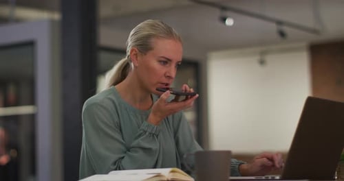 Woman Using Laptop and Talking on Phone in Office
