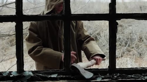 a Man in a Long Cloak with a Hood Walks in an Abandoned Building with Bloody Ax