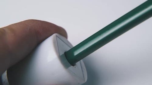 Person Puts Green Pencil Into Sharpener on Light Background