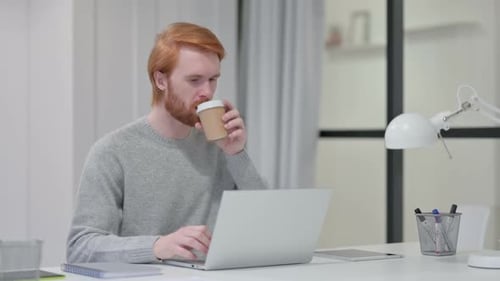 Beard Redhead Man trinkt Kaffee beim Tippen auf Laptop