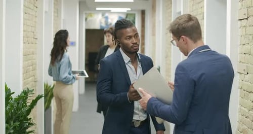 African American and Caucasian Coworkers Discussing Project in Office Corridor. Confident Men
