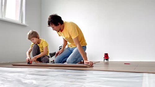 Boy and Adult Installing Flooring Together Indoors