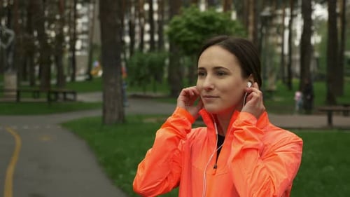 Happy sport woman put on earphones and use smartphone before running training in the park