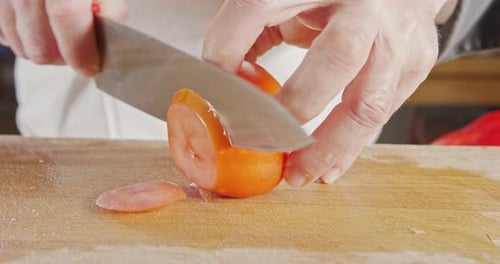 Slow motion close up of a chef knife slicing a tomato
