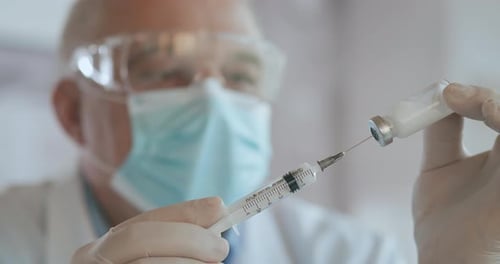 Close Up Shot of Unrecognizable Nurse or Doctor in Gloves Filling Syringe From Ampule with Covid-19