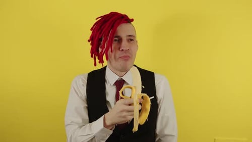 Young Man in White Shirt Vest and Tie Eating Banana on Yellow Background in Studio