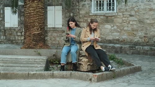 Two woman in coats outdoors in spring time looking in to a smartphone