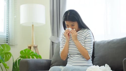 Asian beautiful woman having running nose and sneezing in living room.
