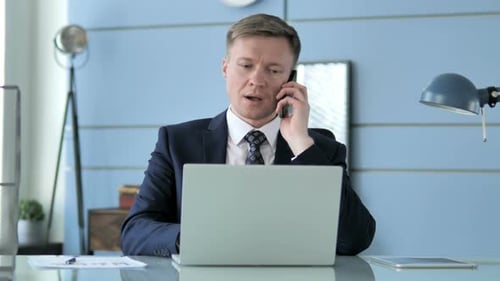 Man in Suit Works at Desk with Laptop and Phone