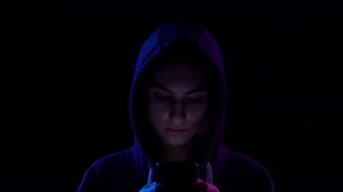 A Young Woman in a Hood with a Phone in Her Hands Closeup. Hacker Makes a Hack Through the Phone