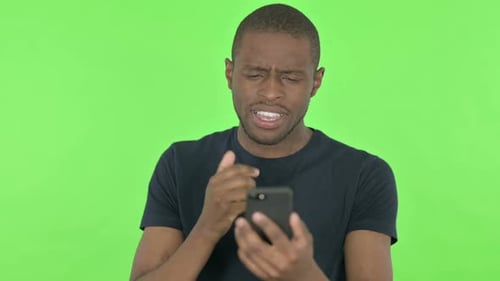 Young African Man Loss on Smartphone on Green Background