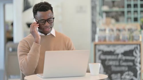 Man talking on smartphone with laptop at table