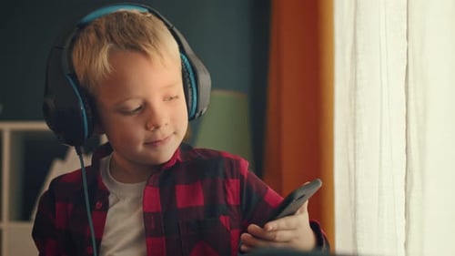 Child Listens with Headphones and Phone Indoors