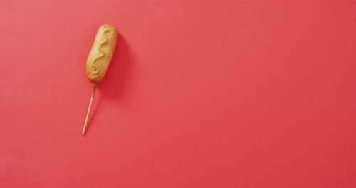 Video of corn dog with mustard on a red surface