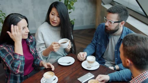 Happy Youth Girls and Guys Chatting and Drinking Coffee at Table in Cafe